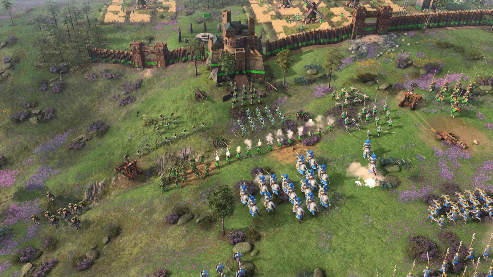 Scottish green-clad units and siege weapons defend a fortified settlement against blue cavalry in an official Age of Empires IV screenshot.