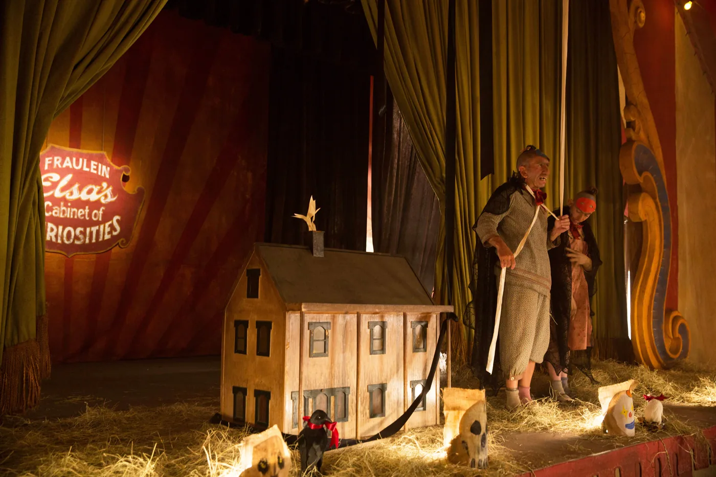 A small model house sits on the stage beside a sign for Fraulein Elsa's Cabinet of Curiosities in a Freak Show publicity still.