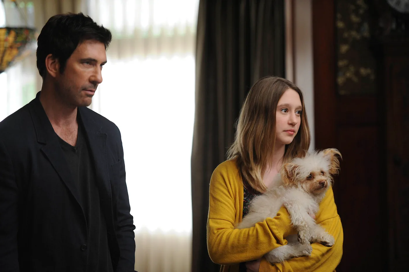 Dylan McDermott as Ben Harmon stands beside Taissa Farmiga as Violet, who holds a small white dog, in a Murder House publicity photo.