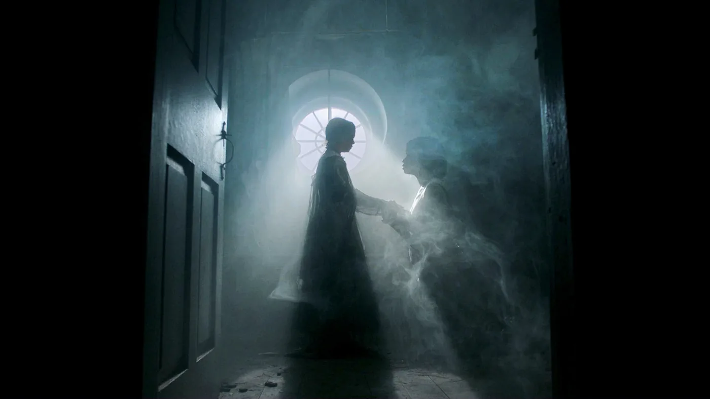 Two figures face each other in silhouette in a misty hallway before a round window in a Roanoke publicity image.