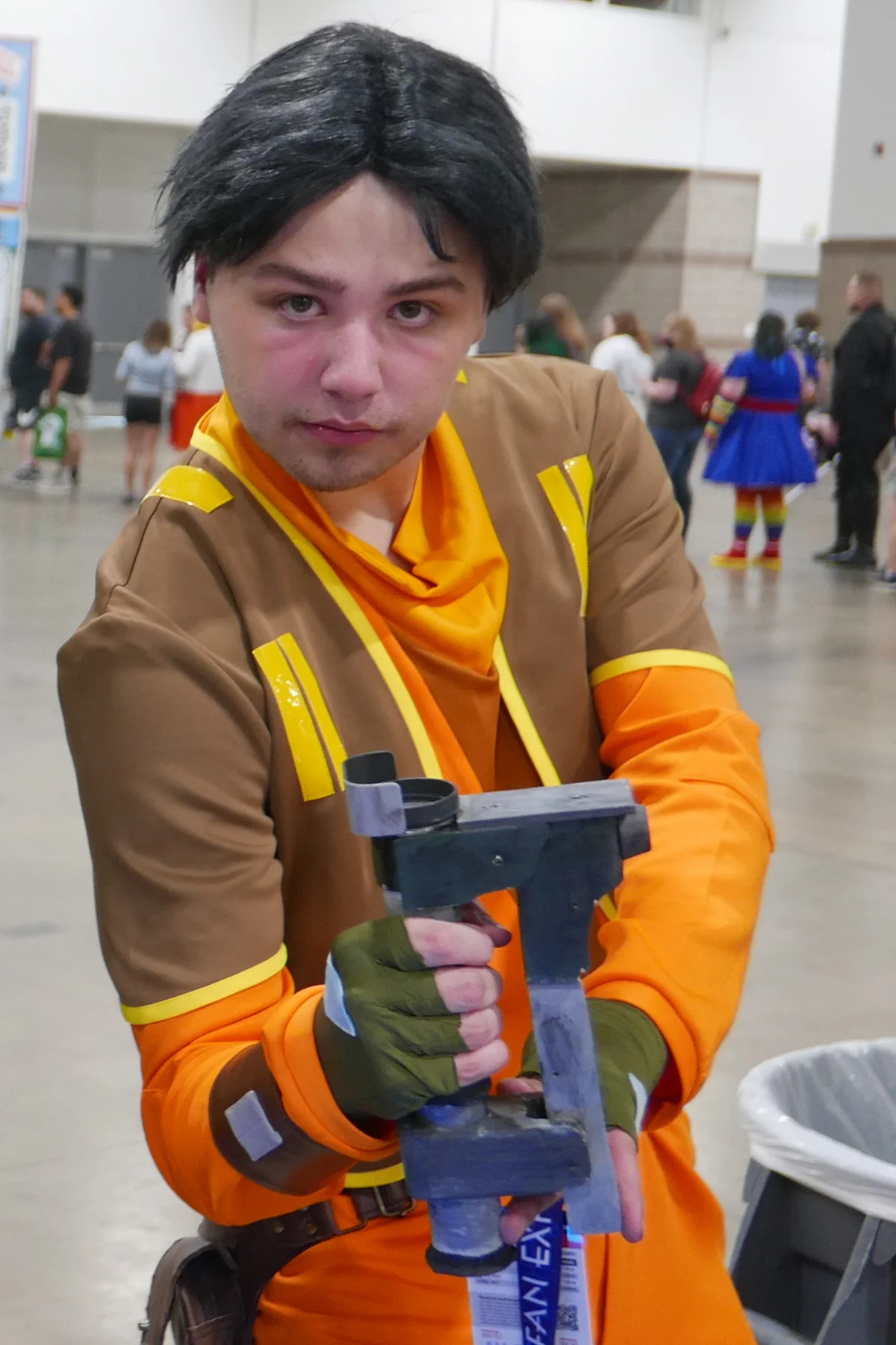 An Ezra Bridger cosplayer in an orange and brown costume holding a prop at Fan Expo Denver 2024.