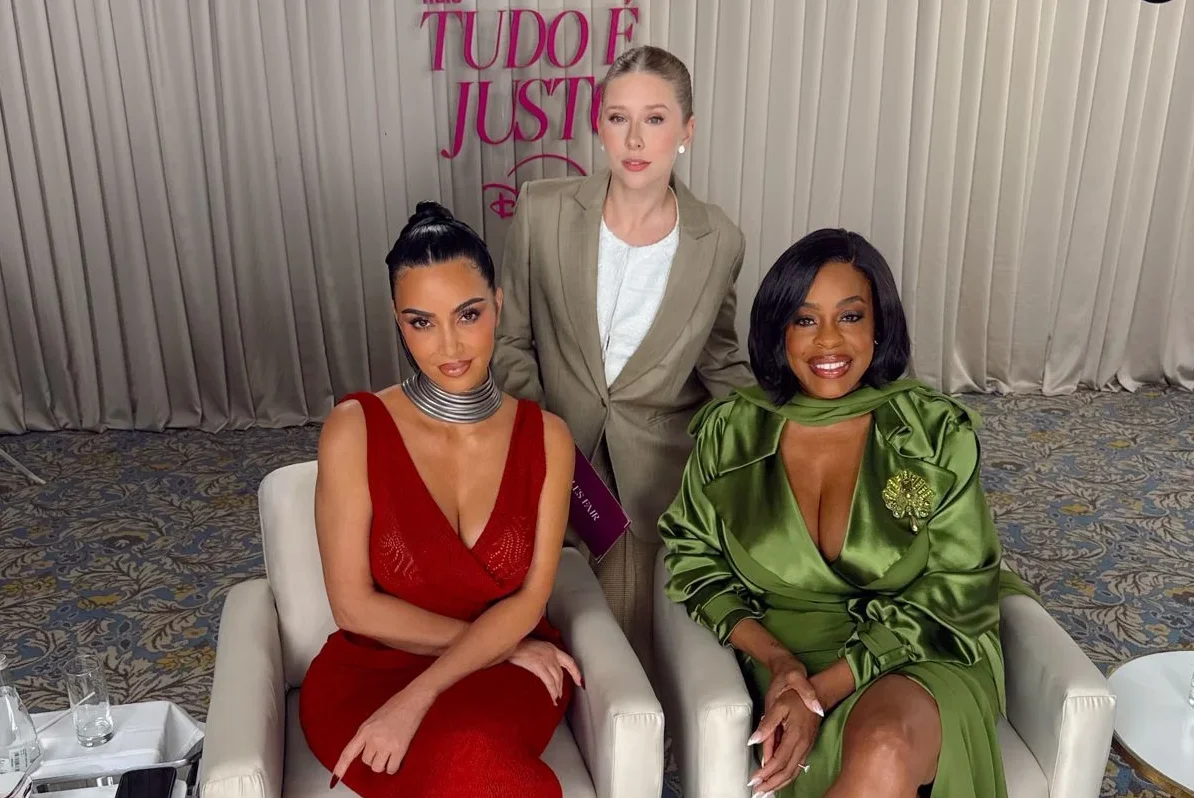 Kim Kardashian in a red dress and Niecy Nash in green seated beside Cela Lopes at an All's Fair promotional appearance.