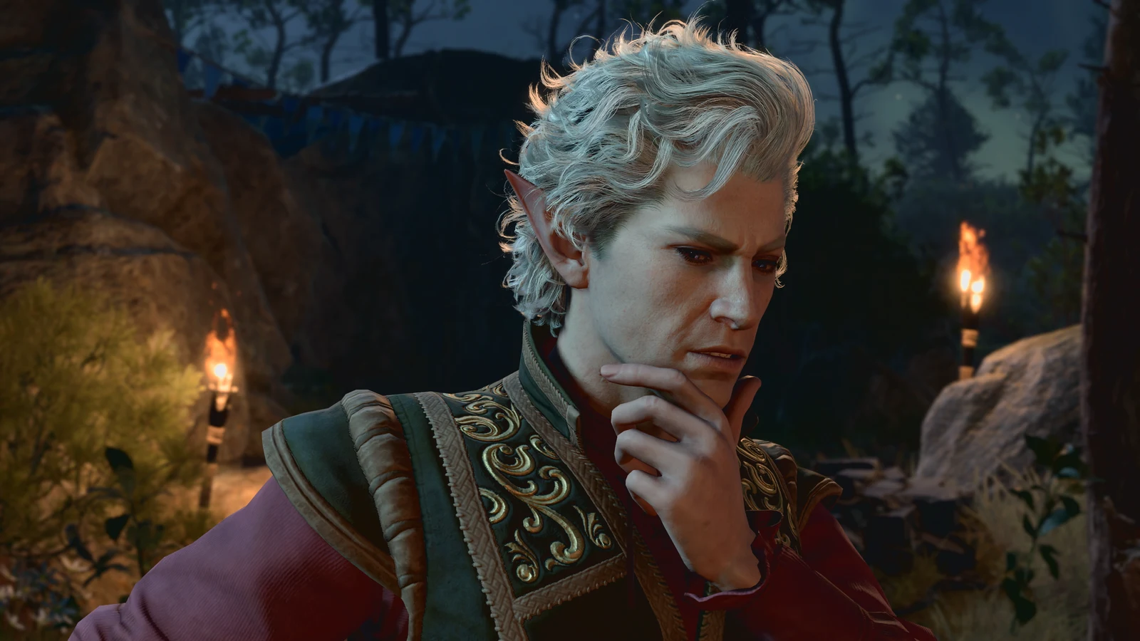 Astarion considering something with his hand at his chin in a torchlit stone setting in Baldur's Gate 3.