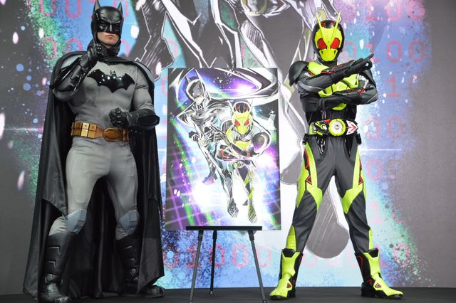 Costumed Batman and Kamen Rider Zero-One performers stand on stage beside the first-look collaboration illustration at the Batman Day 2026 'Rule the Night' event in Tokyo.