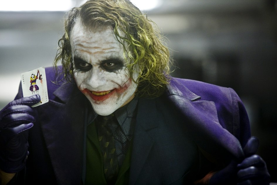 Heath Ledger as the Joker holding a playing card in an official The Dark Knight still.