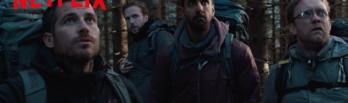 Four hikers with backpacks stand together in a shadowy forest in The Ritual.