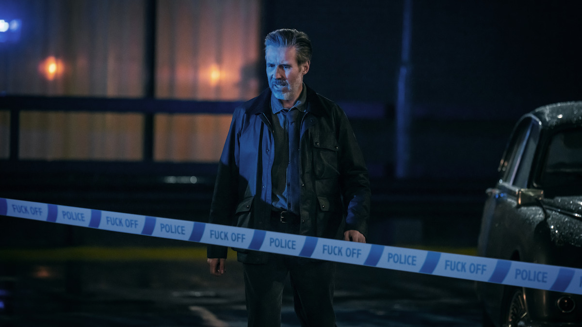 A man stands behind blue police tape outside a building at night in Netflix's first-look image for Blackmere.