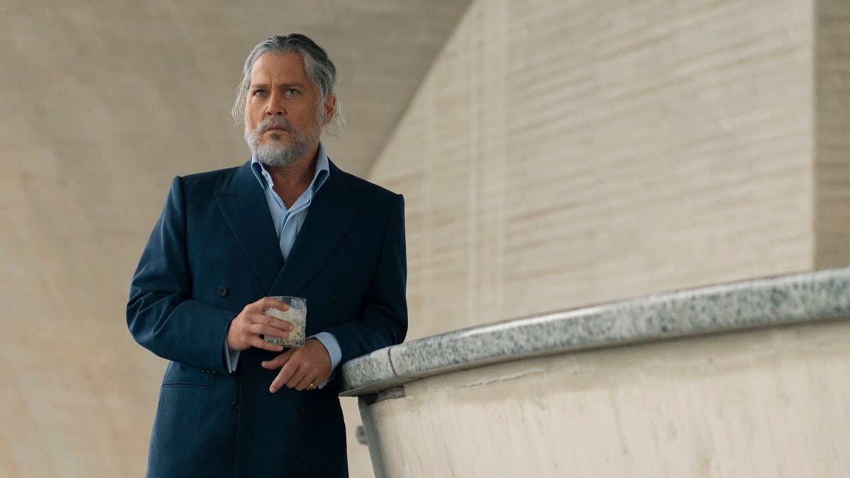 Johnny Depp in character for Day Drinker, with gray hair and beard, a dark suit and a drink in his hand.
