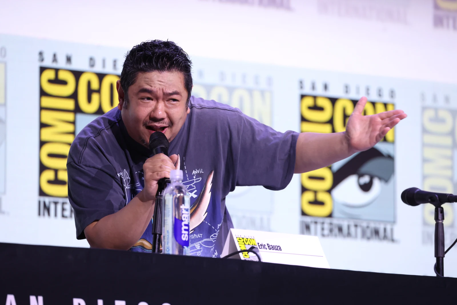 Eric Bauza speaking into a microphone and gesturing during the Coyote vs. Acme panel at San Diego Comic-Con in July 2025.
