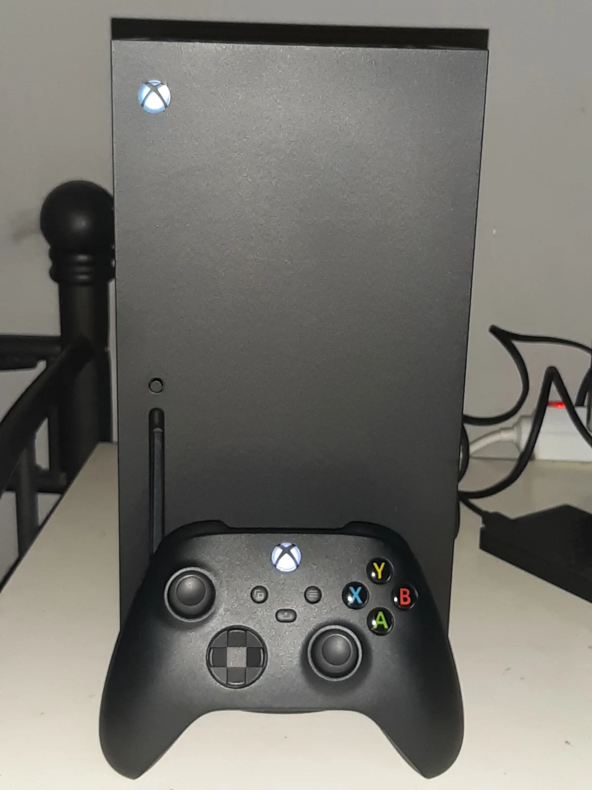 A black Xbox Series X console with its wireless controller on a light-colored desk.