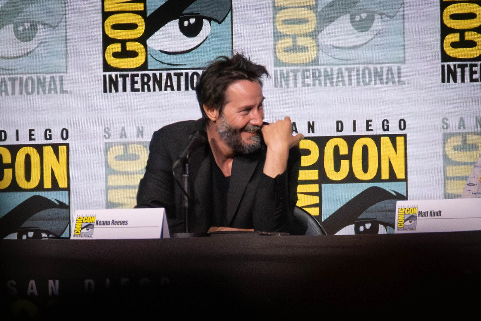 Keanu Reeves smiling behind a panel table at San Diego Comic-Con in July 2024.