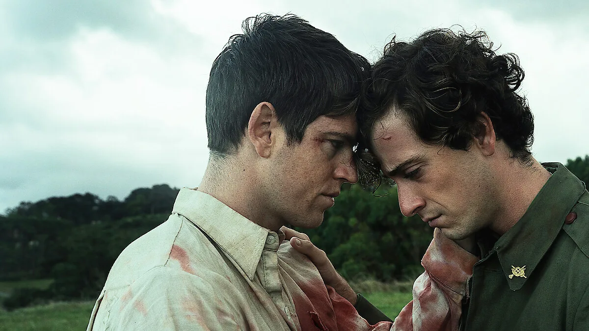 Two injured men in bloodied clothes touch foreheads in a field in an official La Bola Negra promotional still.