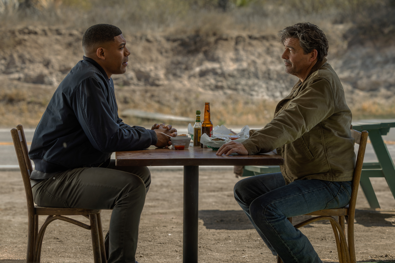 John Stewart and Hal Jordan sit across from each other at an outdoor table in Lanterns Episode 1.