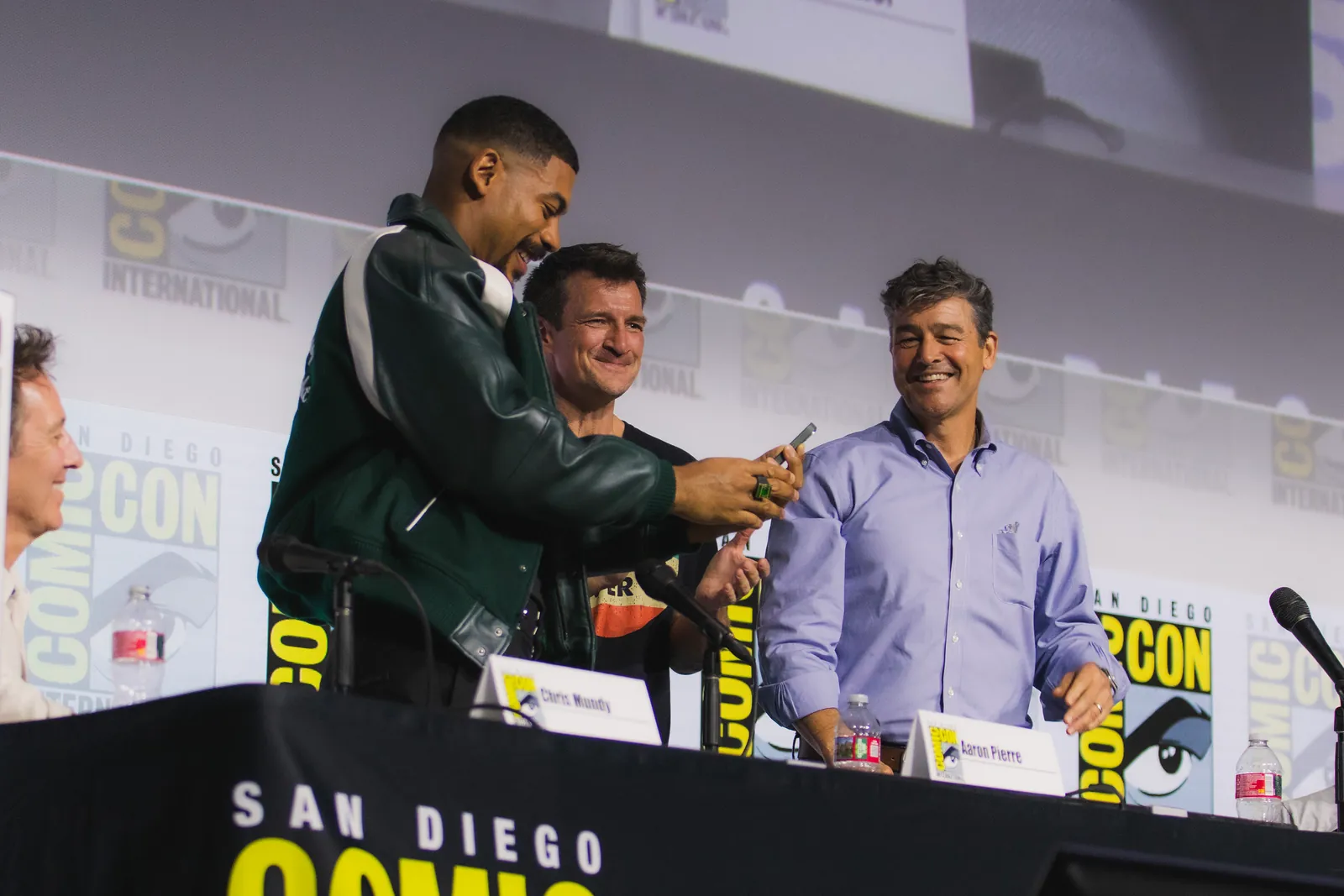 Aaron Pierre, Nathan Fillion and Kyle Chandler smiling on the Lanterns panel stage at San Diego Comic-Con in 2026.
