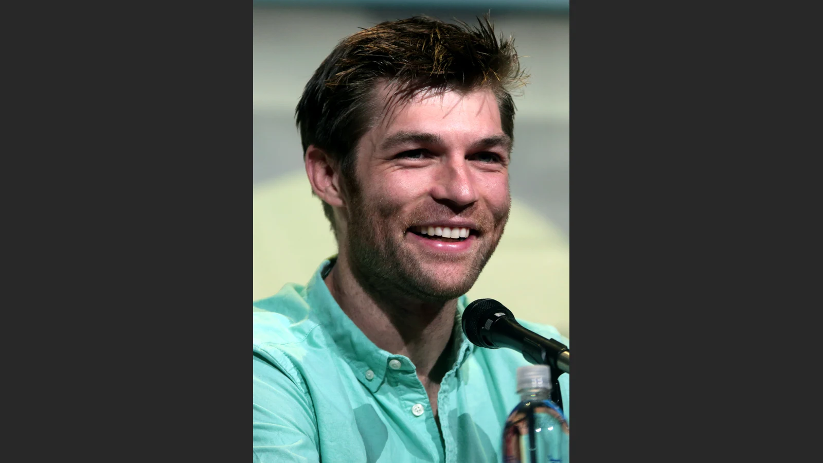 Liam McIntyre smiling at San Diego Comic-Con in 2016, with his portrait fitted inside a neutral frame.