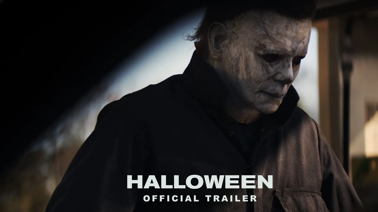 Michael Myers in his worn pale mask, head lowered, from the official 2018 Halloween film trailer thumbnail.