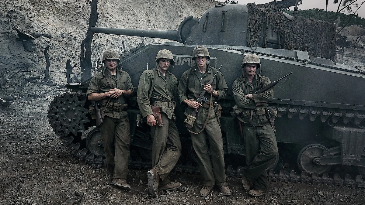Four Marines in WWII uniforms standing in front of a tank in a smoky, war-torn environment, official still from Netflix's The Mosquito Bowl.
