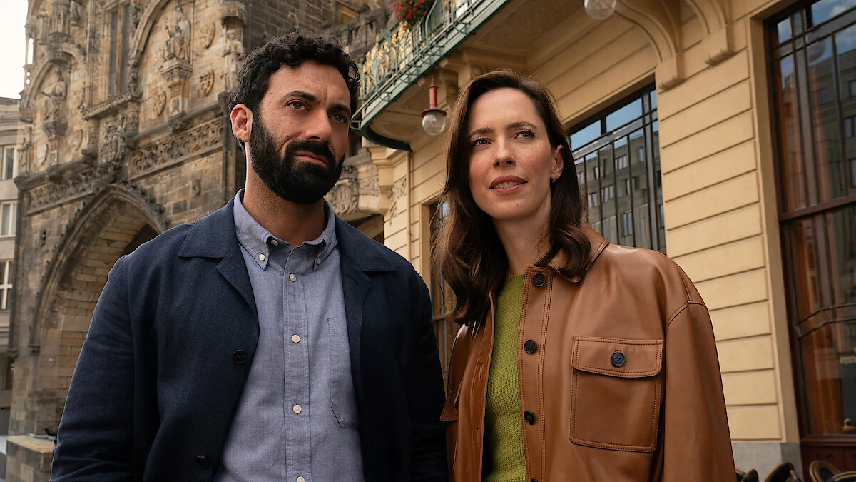 Morgan Spector as Robert Langdon and Rebecca Hall as Katherine Solomon standing together on a Prague street during production of Netflix's untitled Robert Langdon series.