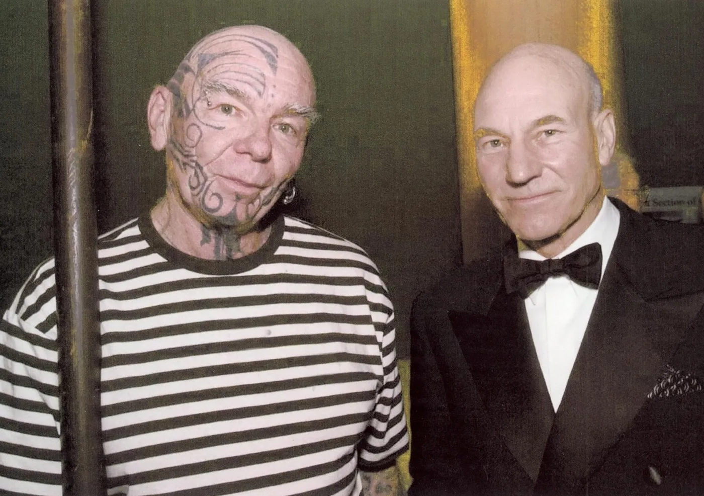 Patrick Stewart standing beside a park volunteer holding a whaling harpoon at San Francisco Maritime National Historical Park.