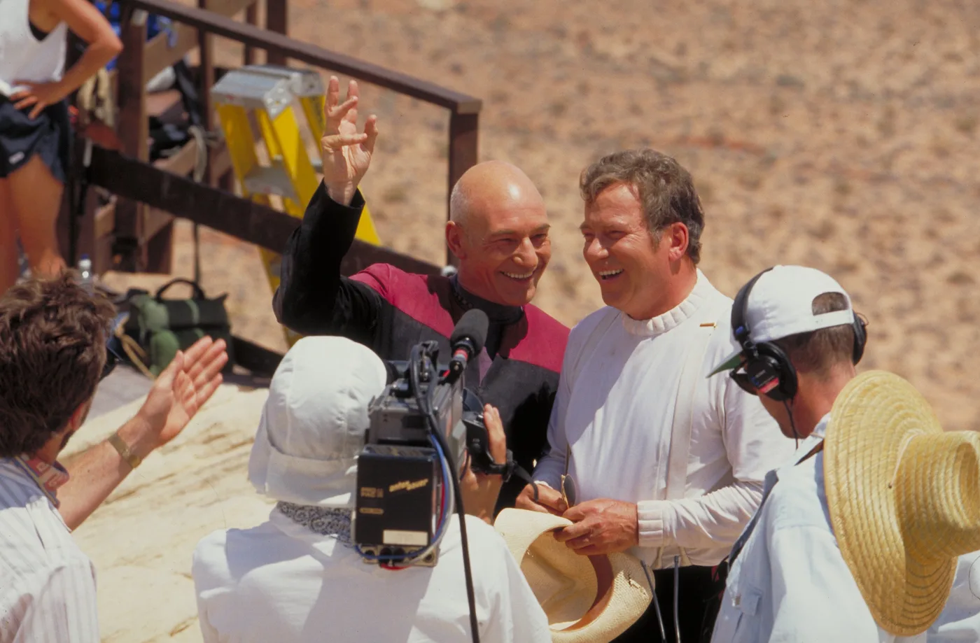 Patrick Stewart and William Shatner laughing together on location while a camera crew films them during production of Star Trek Generations.
