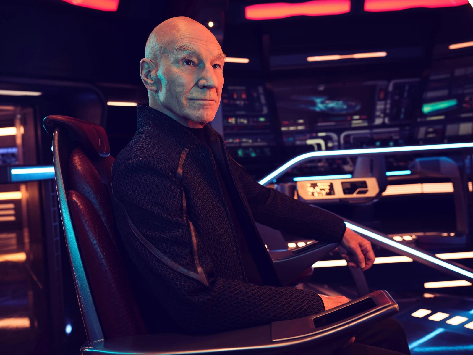 Patrick Stewart as Jean-Luc Picard, seated on a starship bridge in an official promotional photograph for Star Trek: Picard season three.