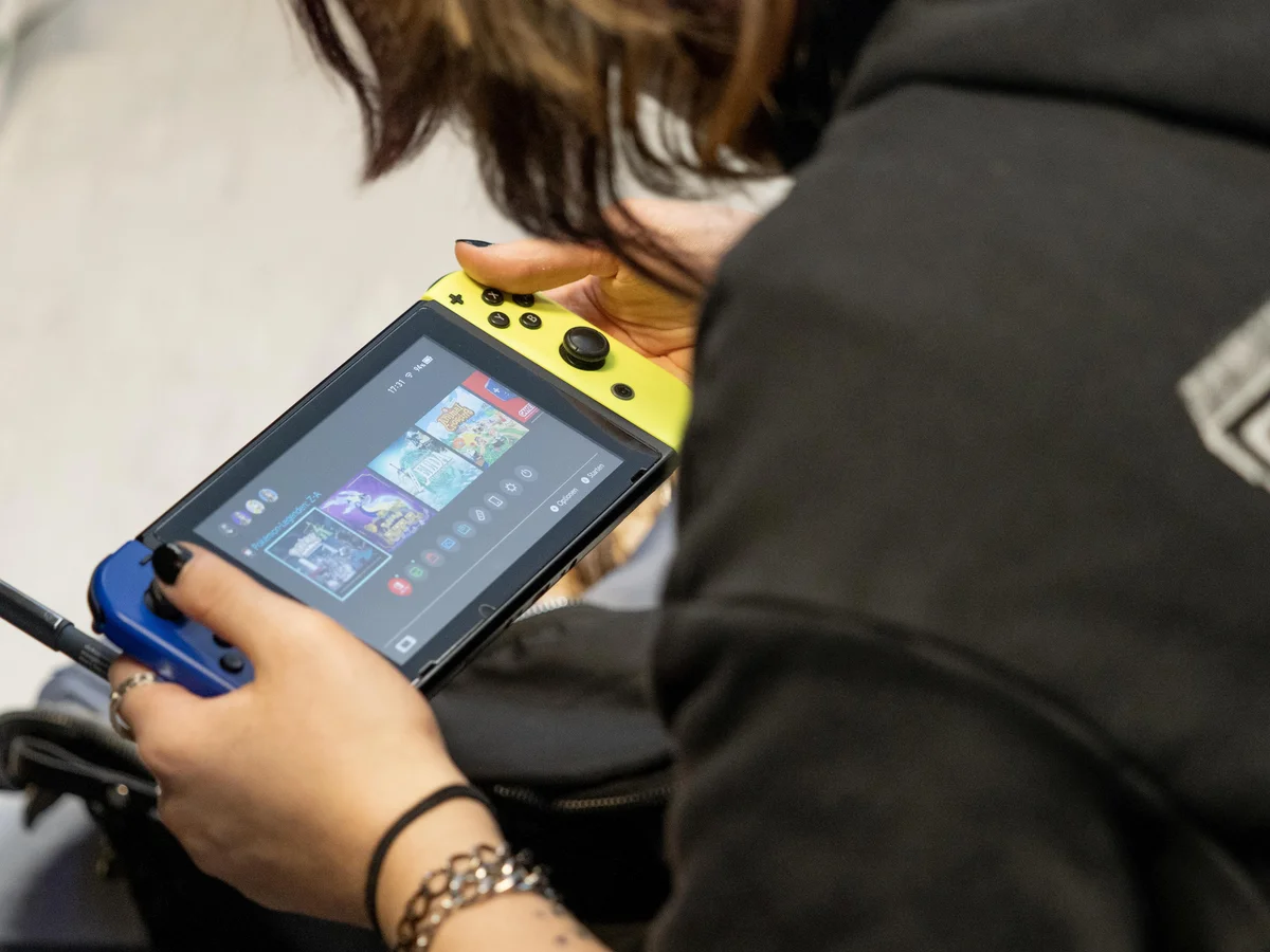 A person holding a Nintendo Switch on its home menu, with Pokémon game icons visible.