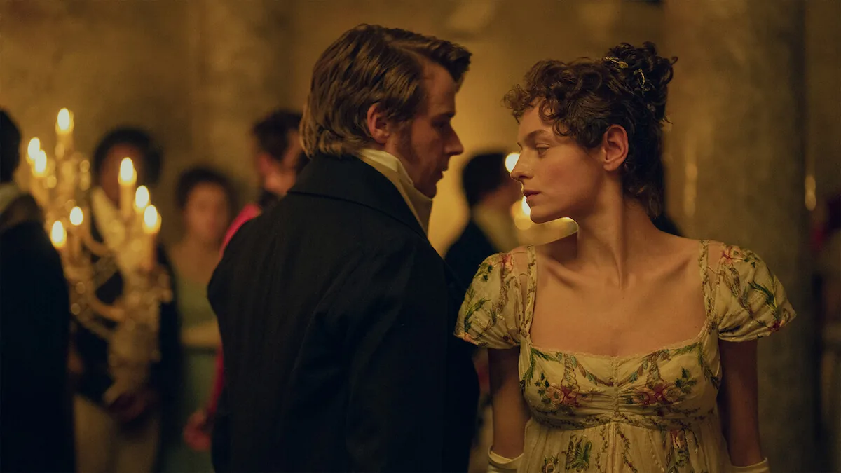 Emma Corrin as Elizabeth Bennet and Jack Lowden as Mr. Darcy face each other in candlelight at a ball in Netflix's Pride and Prejudice.