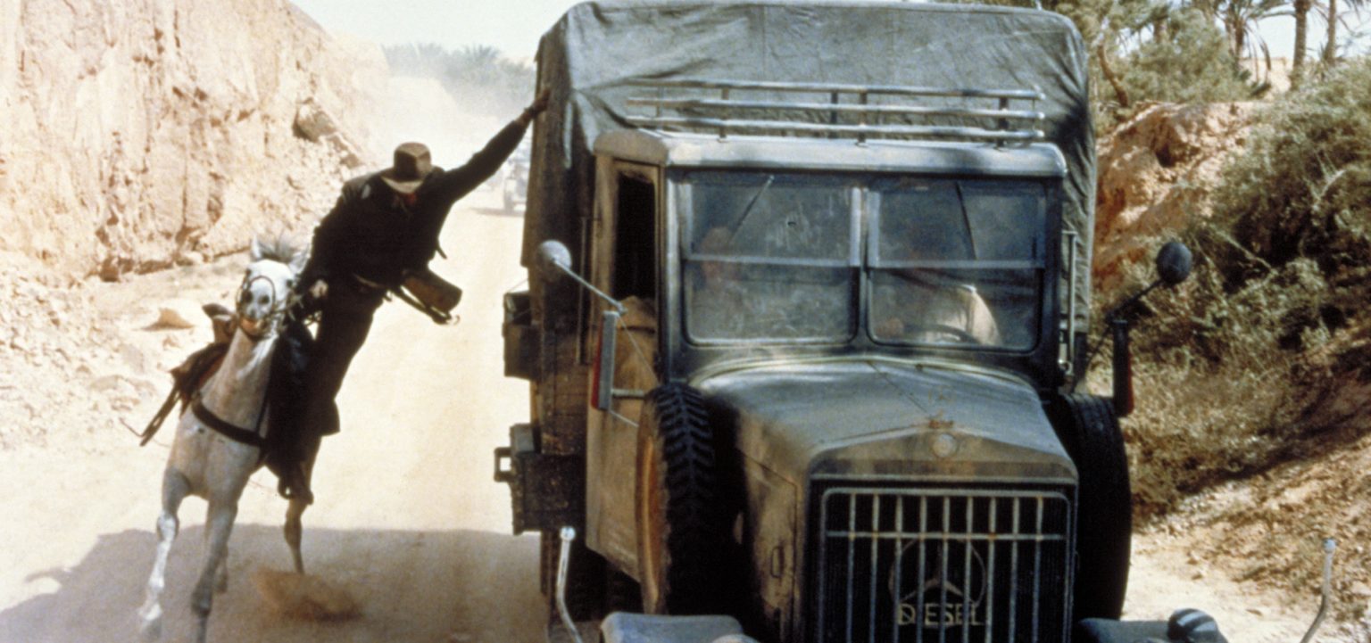 Indiana Jones rides beside a truck during the Raiders of the Lost Ark pursuit.