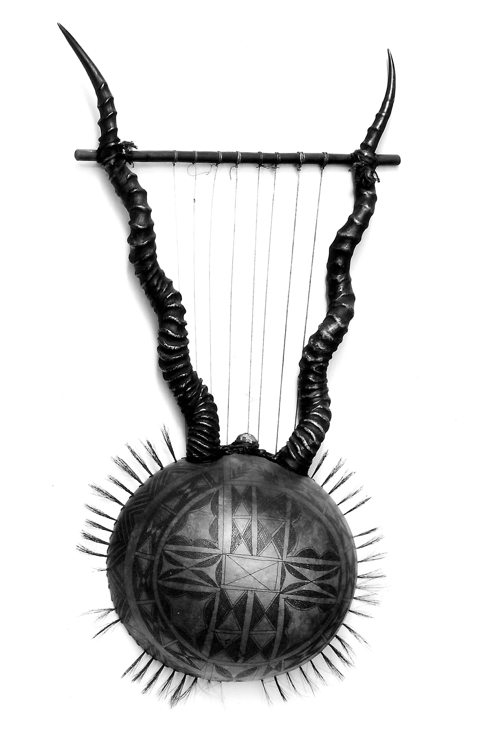 Black and white photograph of a bowl lyre with horn arms, hanging strings and a patterned round body.