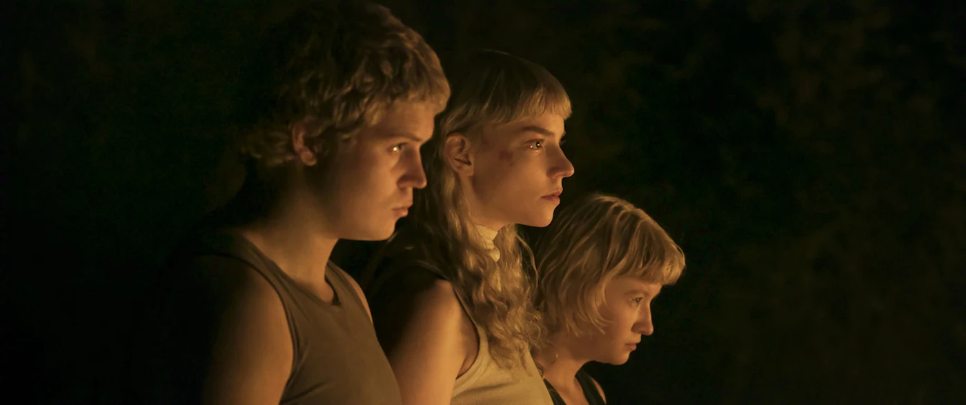 Yung Lean as Arthur, Anya Taylor-Joy as Joan, and Jade Croot as Louise standing together in firelight in Netflix's Sacrifice.