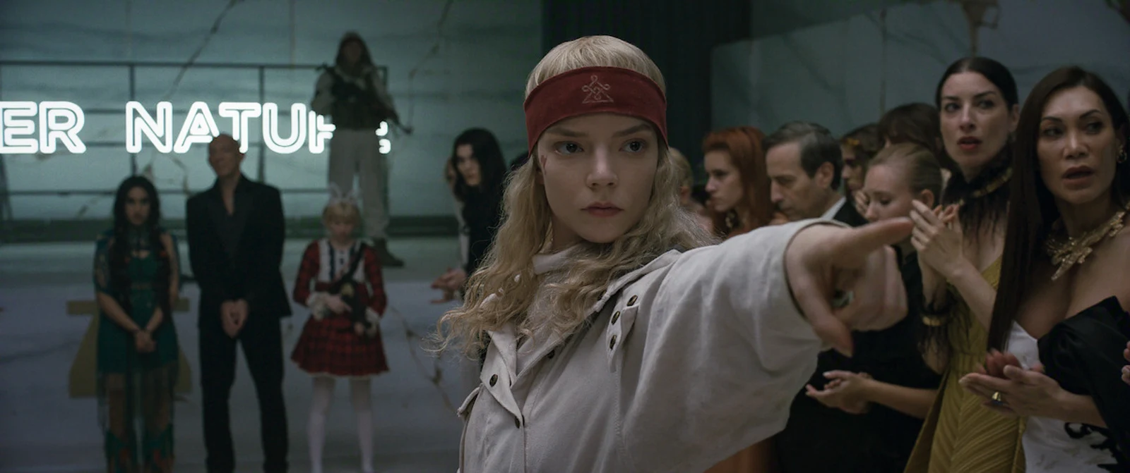 Anya Taylor-Joy as Joan pointing at a hostage during the gala takeover in Netflix's Sacrifice, with captured guests and a masked follower behind her.