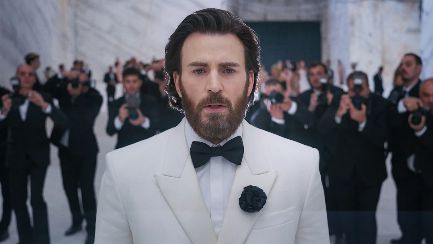 Chris Evans as Mike Tyler in a white tuxedo, surrounded by photographers at the Sacrifice gala entrance.