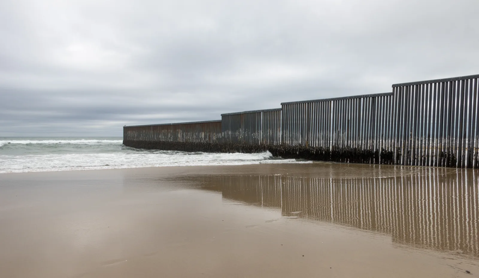 The Mexico–US border fence extending across the beach and into the Pacific Ocean at Tijuana.