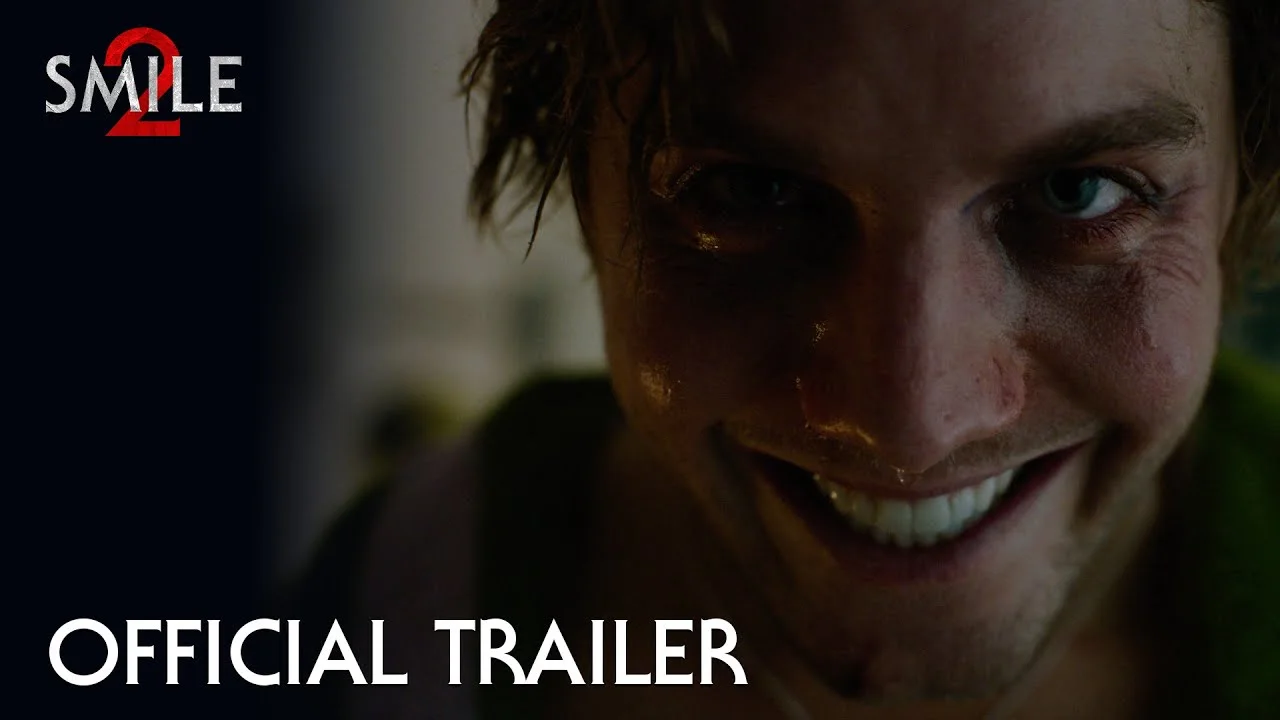 Close-up of a sweating man with a fixed wide smile in Paramount's official Smile 2 trailer thumbnail, beside the Smile 2 logo and the words Official Trailer.