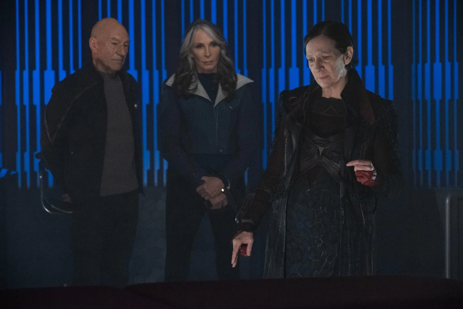 Picard and Beverly Crusher standing before the villain Vadic in a dark blue-lit room in the Star Trek: Picard episode Dominion.