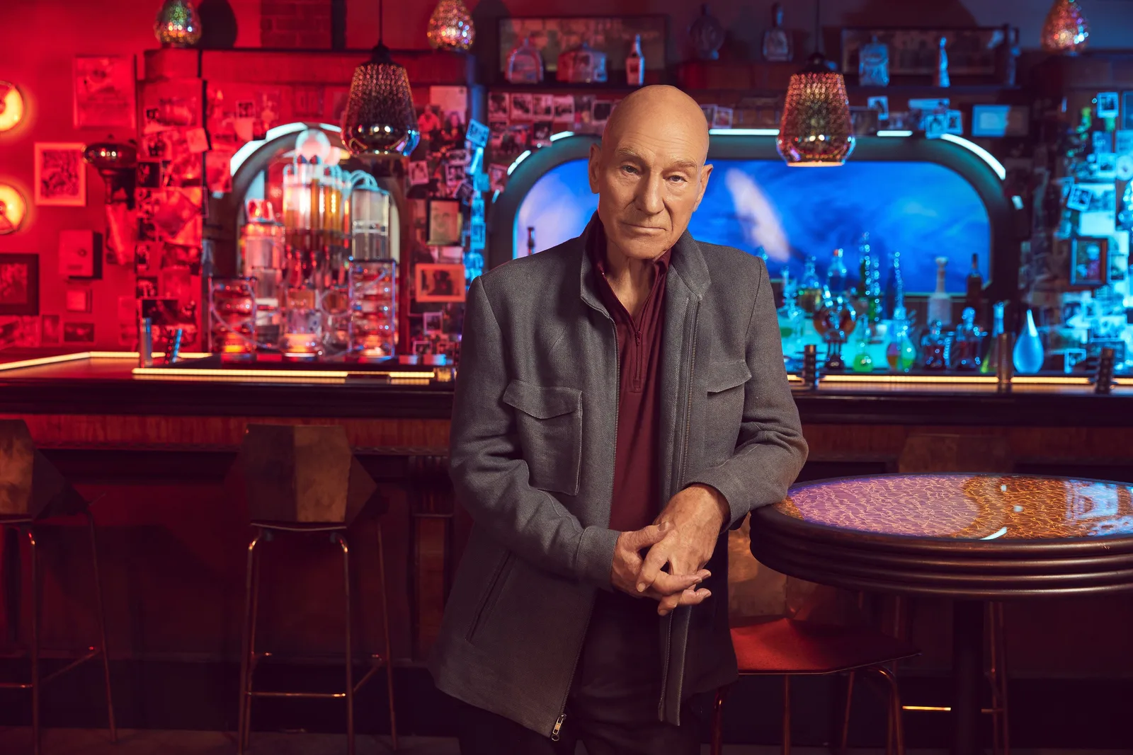 Patrick Stewart as Picard leaning against a table in a red-lit bar set in a promotional photograph for season two of Star Trek: Picard.