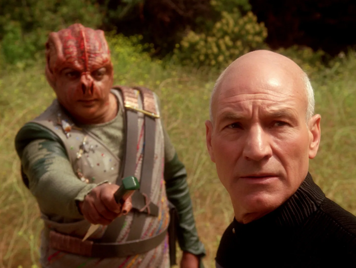 Dathon, a Tamarian captain, holds out a dagger toward Captain Picard on the surface of El-Adrel IV in the TNG episode Darmok.