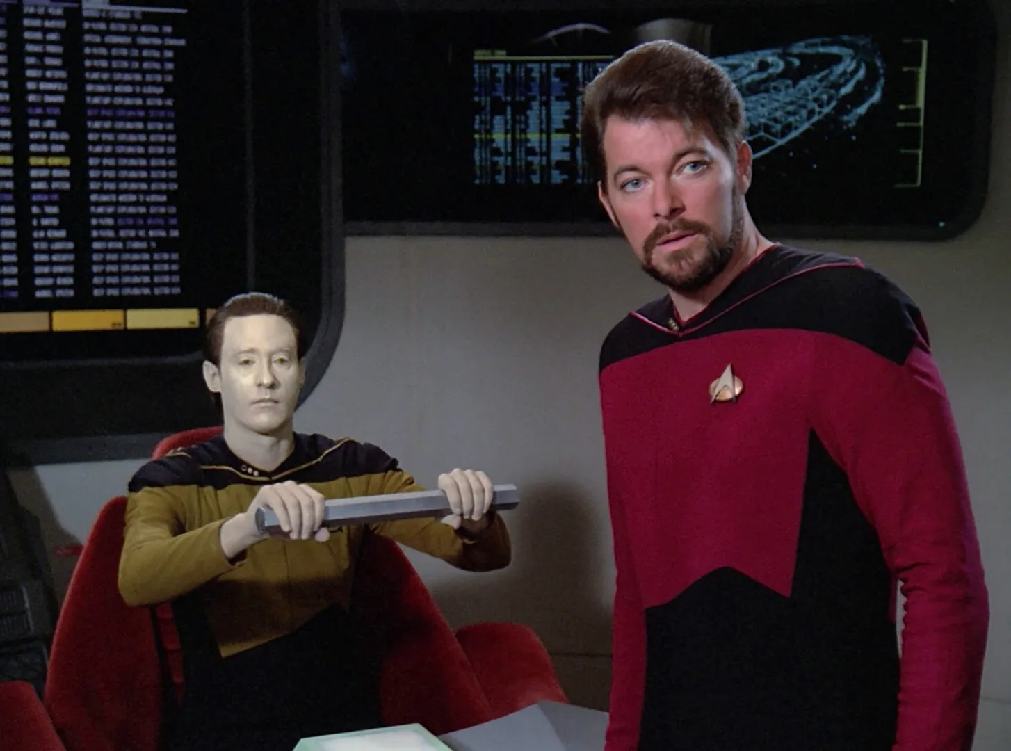 Data holds up a metal rod while Commander Riker stands beside him in the hearing room in The Measure of a Man.
