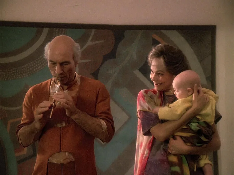 Picard, living as Kamin, plays a flute beside his wife Eline, who holds their young son.