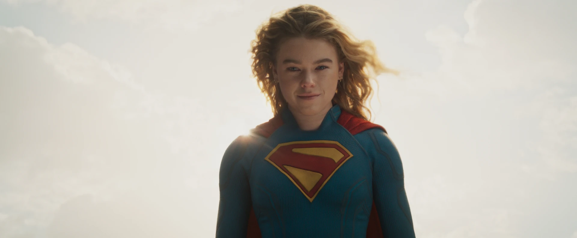Milly Alcock as Kara Zor-El in costume against a bright sky in official Supergirl imagery.