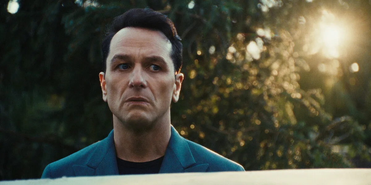 Matthew Rhys as Nile Jarvis looks over a wall in warm backlight in a Season 1 still from Netflix's The Beast in Me.