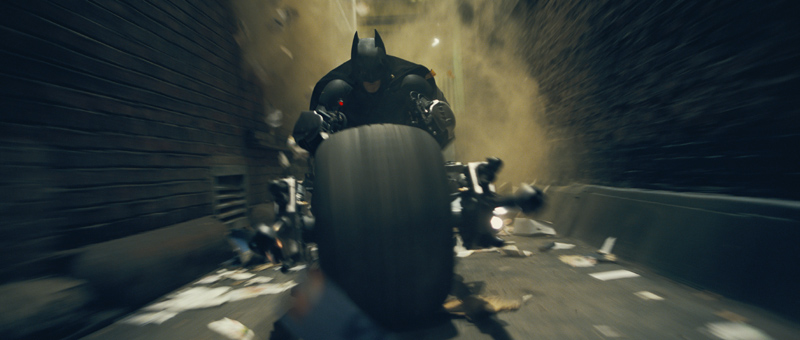 Batman rides the Batpod through debris in an official The Dark Knight publicity image.