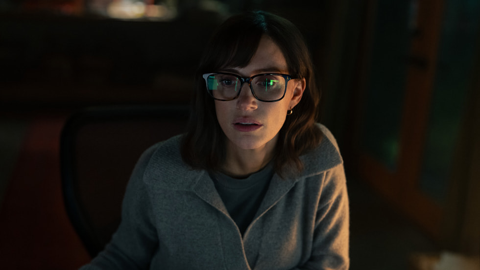 Apple TV Jessica Chastain as Jodi Goodwin in The Savant, sitting at a desk in low light, wearing glasses with a data reflection visible in the lenses.