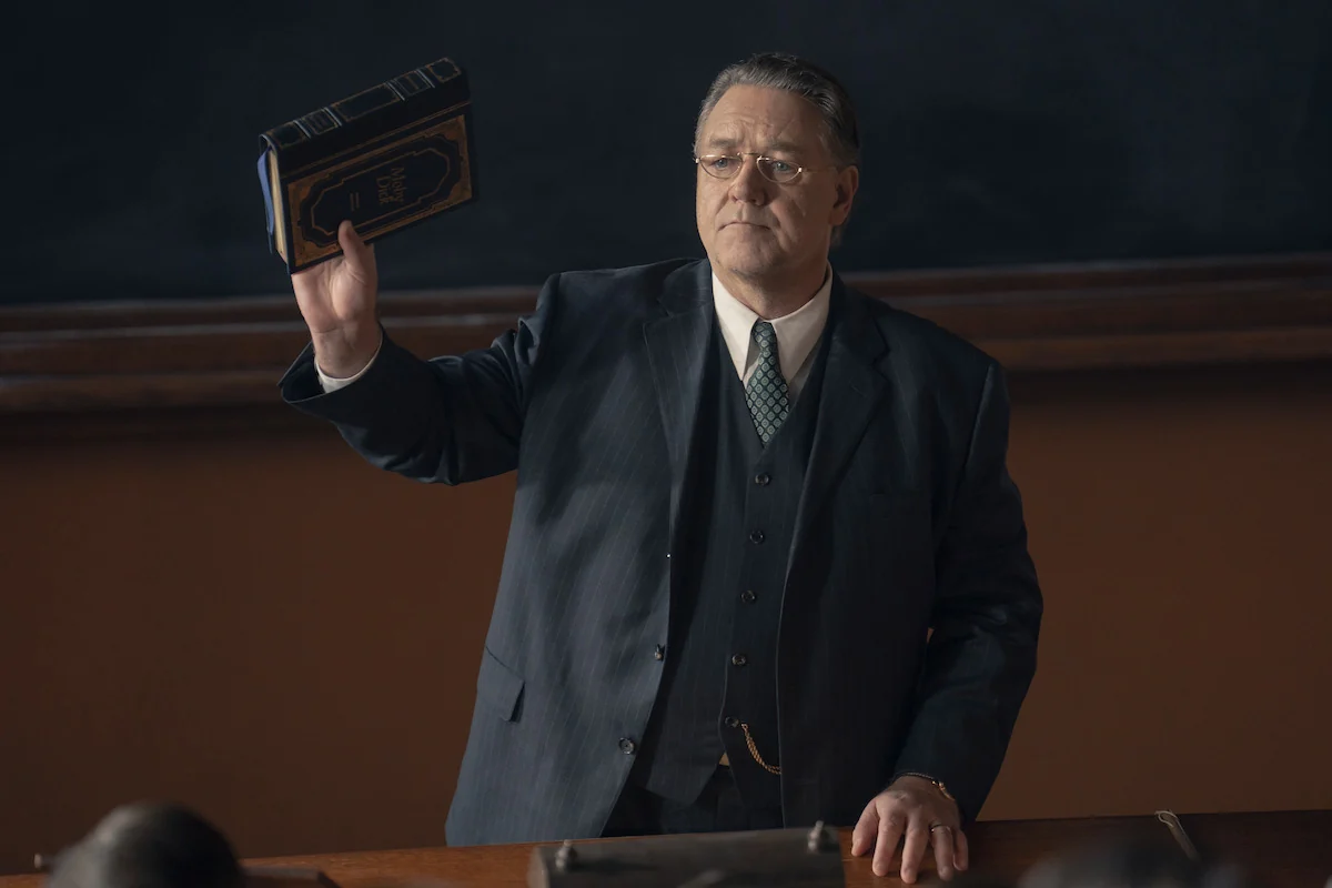 Russell Crowe as Henry Murray holds a copy of Moby-Dick in a classroom in Netflix’s UNABOMBER.