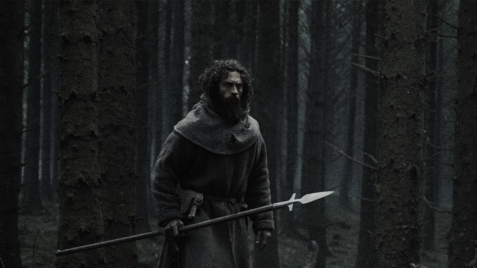 A cloaked man carrying a long spear through a dark forest in official Werwulf artwork.