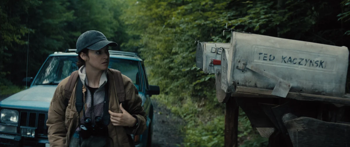 Shailene Woodley as fictional FBI agent Joanne Miller stands beside a mailbox marked Ted Kaczynski in a wooded setting in UNABOMBER.