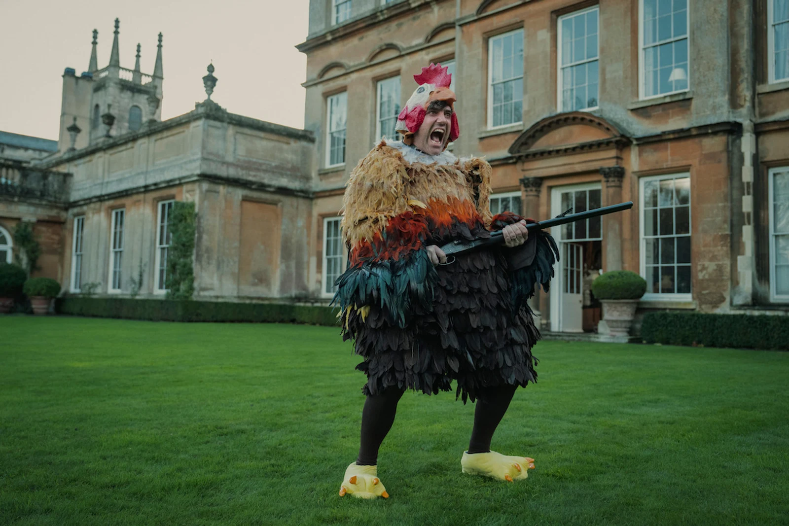 Daniel Ings as Freddy Horniman wearing a chicken costume and holding a shotgun in Season 1 of The Gentlemen.