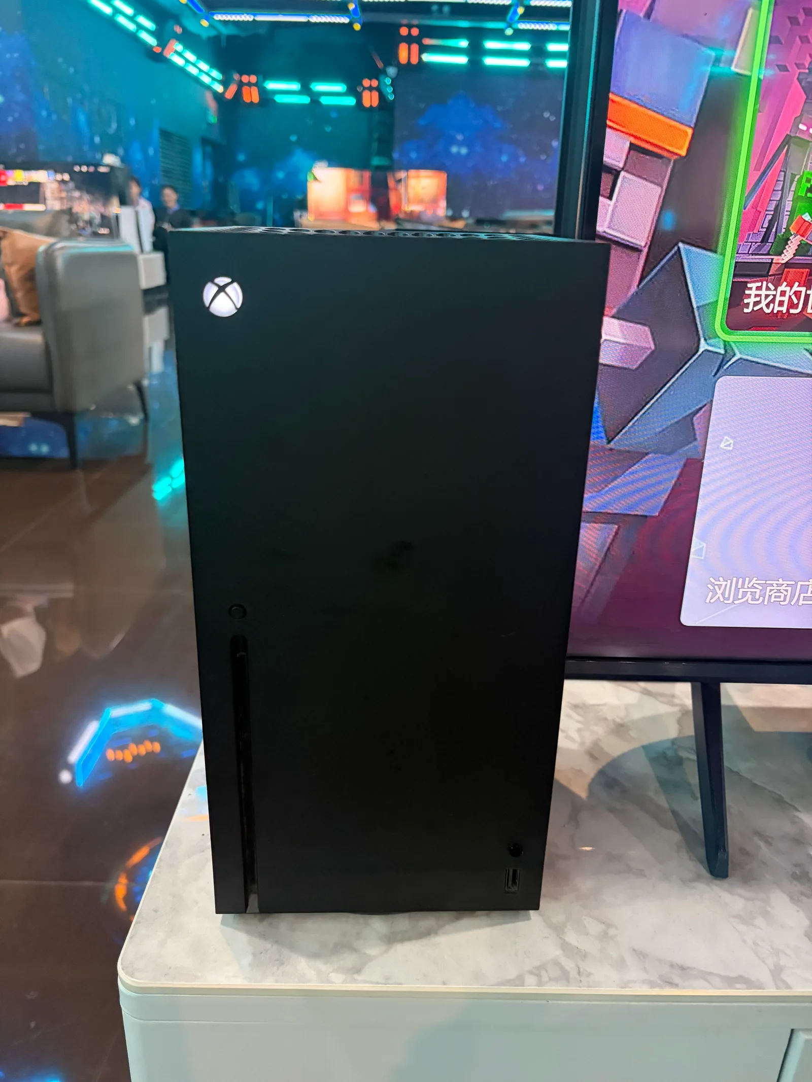 A black Xbox Series X console standing on a counter beside a display.